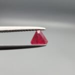 ​A 0.55 carat natural red Ruby (Yaqoot) from Kabul, Afghanistan, featuring a sharp triangle cut with rich color and natural internal silk, held in jeweler's tweezers.