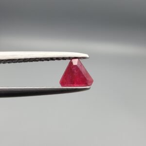 ​A 0.55 carat natural red Ruby (Yaqoot) from Kabul, Afghanistan, featuring a sharp triangle cut with rich color and natural internal silk, held in jeweler's tweezers.