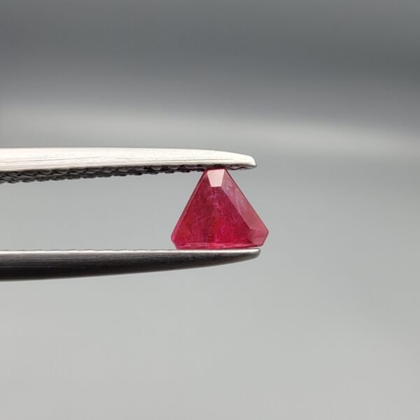 ​A 0.55 carat natural red Ruby (Yaqoot) from Kabul, Afghanistan, featuring a sharp triangle cut with rich color and natural internal silk, held in jeweler's tweezers.