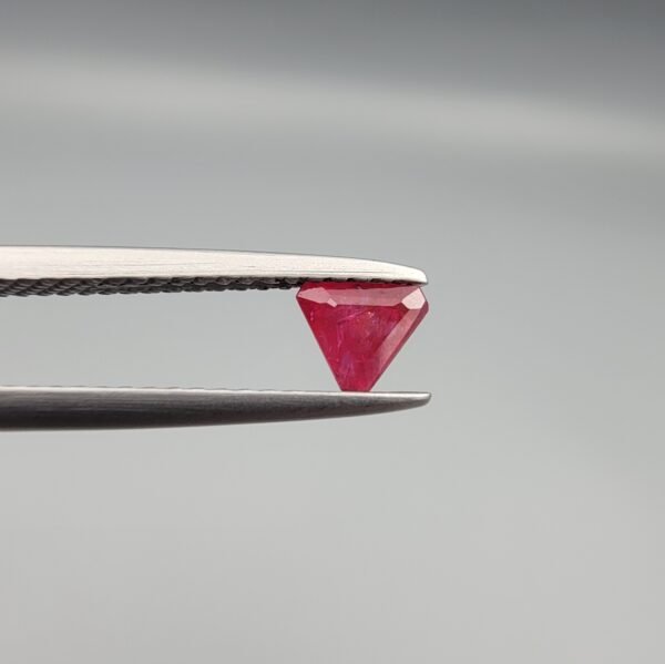​A 0.55 carat natural red Ruby (Yaqoot) from Kabul, Afghanistan, featuring a sharp triangle cut with rich color and natural internal silk, held in jeweler's tweezers.