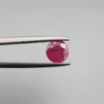 ​A 0.59 carat natural red Ruby (Yaqoot) from Kabul, Afghanistan, with a brilliant round cut, showcasing natural internal silk and vibrant saturation, held in jeweler's tweezers.