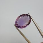 Natural Amethyst Katela gemstone oval cut, 9.85 carat weight, light purple color, transparent Brazilian amethyst held with tweezers.