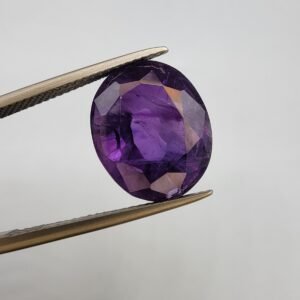 Natural Amethyst Katela gemstone 10.43 carats from Brazil showing deep purple color with natural inclusions, oval faceted cut held in tweezers