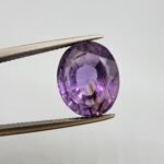 Natural Amethyst Katela gemstone 10.21 carats from Brazil with light purple color, oval faceted cut and visible natural inclusions held in tweezers