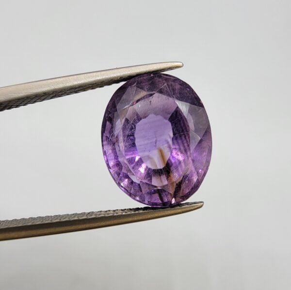 Natural Amethyst Katela gemstone 10.21 carats from Brazil with light purple color, oval faceted cut and visible natural inclusions held in tweezers