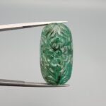 Massive 32.08 carat natural green emerald gemstone, intricate hand-carved floral design from Zambia, held in professional jewelry tweezers.