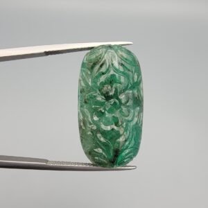 Massive 32.08 carat natural green emerald gemstone, intricate hand-carved floral design from Zambia, held in professional jewelry tweezers.