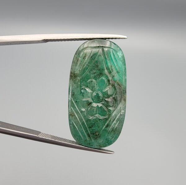 Massive 32.08 carat natural green emerald gemstone, intricate hand-carved floral design from Zambia, held in professional jewelry tweezers.