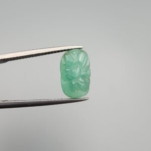 Intricately hand-carved natural green emerald gemstone, 3.12 carats, featuring a floral motif from Zambia, held in professional jewelry tweezers.