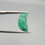 Exquisite hand-carved natural green emerald gemstone, 6.33 carats, featuring a detailed floral pattern from Zambia, held in professional jewelry tweezers.