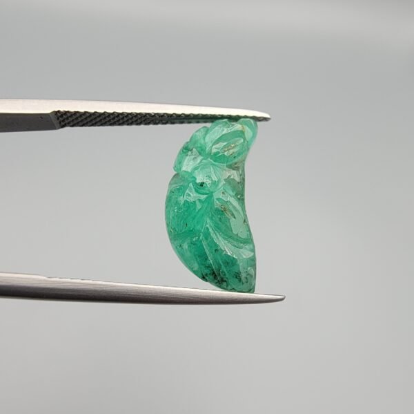 Exquisite hand-carved natural green emerald gemstone, 6.33 carats, featuring a detailed floral pattern from Zambia, held in professional jewelry tweezers.