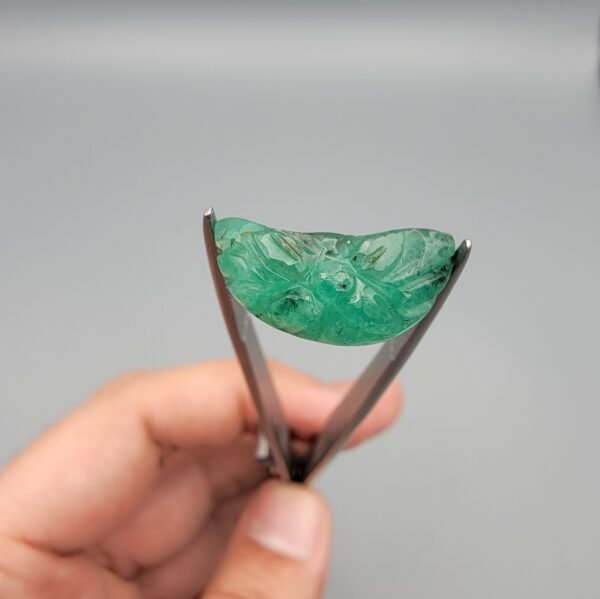 Exquisite hand-carved natural green emerald gemstone, 6.33 carats, featuring a detailed floral pattern from Zambia, held in professional jewelry tweezers.
