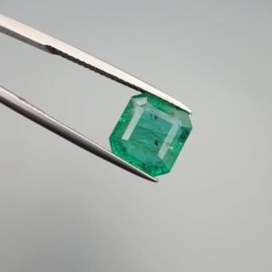 Octagon step cut natural green emerald gemstone, 3.40 carats, ethically sourced from Zambia, held in professional jewelry tweezers.