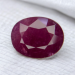 Natural Mozambique Ruby yaqoot gemstone 7.70 carat oval faceted cut showing deep purplish red color held with tweezers on white background