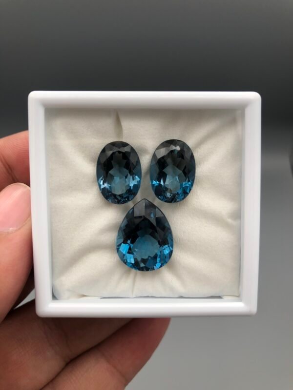High-grade 28.33 carat total weight natural London Blue Topaz gemstone set, featuring a perfectly matched pair of pear-shaped stones and a central pear-shaped piece for a pendant.