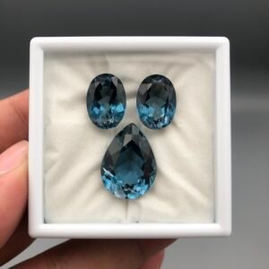 Elite 33.86 carat total weight natural London Blue Topaz gemstone suite, featuring a matched pair of oval-cut stones and a large pear-shaped pendant gem in deep teal-blue.