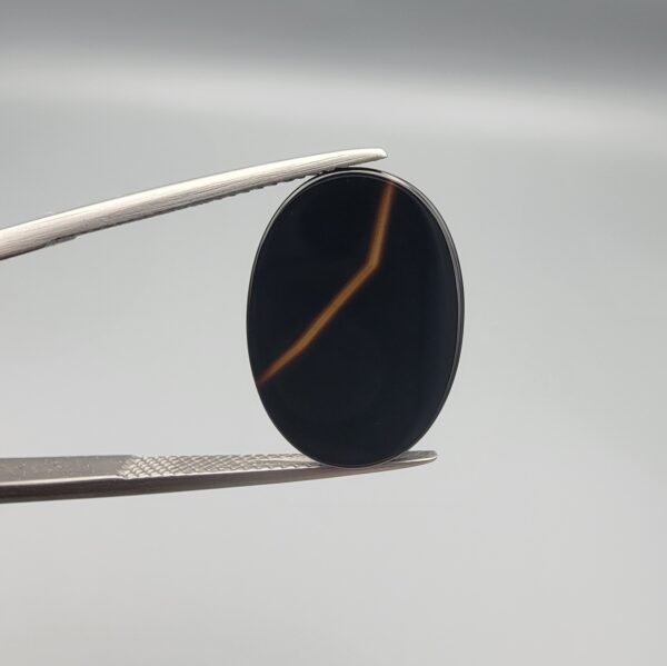 Polished 7.10 carat natural black chalcedony agate (Sulemani Aqeeq) gemstone featuring a smooth oval cabochon cut and a sharp, angular orange-gold banding line.