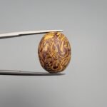 High-luster 20.08 carat natural Calligraphy Stone (Sang-e-Maryam) showcasing dense, intricate yellow and gold fossilized shell patterns against a deep chocolate brown jasper matrix.