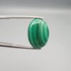 High-polished 21 carat natural malachite (Dana-e-Farhang) gemstone featuring deep emerald green vertical banding and a glossy oval cabochon finish, held in professional gemstone tweezers.