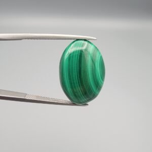 High-polished 21 carat natural malachite (Dana-e-Farhang) gemstone featuring deep emerald green vertical banding and a glossy oval cabochon finish, held in professional gemstone tweezers.