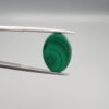High-polished 10.90 carat natural malachite (Dana-e-Farhang) gemstone featuring deep, swirling emerald green orbital patterns in a smooth oval cabochon cut, held in tweezers.