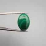 High-polished 10.90 carat natural malachite (Dana-e-Farhang) gemstone featuring deep, swirling emerald green orbital patterns in a smooth oval cabochon cut, held in tweezers.