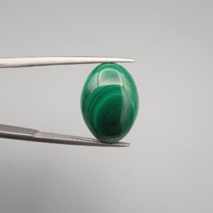High-polished 10.90 carat natural malachite (Dana-e-Farhang) gemstone featuring deep, swirling emerald green orbital patterns in a smooth oval cabochon cut, held in tweezers.