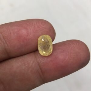 Certified 4.84 carat natural yellow sapphire (Pukhraj) from Sri Lanka, featuring a classic oval shape and visible natural inclusions, shown held between fingers to highlight its scale.