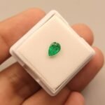Vibrant 0.70 carat natural Swat emerald with a classic pear-shaped brilliant cut, showcasing the signature deep "Swat green" color and characteristic inclusions, presented in a gemstone box.