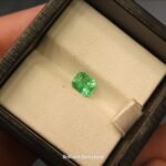 High-clarity 0.84 carat natural Panjshir emerald featuring a classic emerald cut with a luminous mint-to-forest green glow, presented in a black jeweler's display box.
