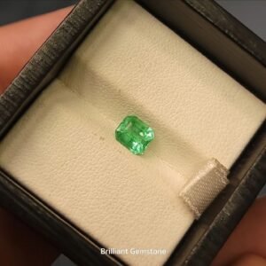 High-clarity 0.84 carat natural Panjshir emerald featuring a classic emerald cut with a luminous mint-to-forest green glow, presented in a black jeweler's display box.