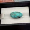 Vibrant 9.73 carat natural Egyptian turquoise (Feroza) oval cabochon featuring a bright sky-blue base with a fine, dark web-like matrix, presented in a black jeweler's display box.