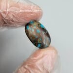 Large 12.70 carat natural Egyptian turquoise (Feroza) oval cabochon with a rich teal-blue body and an intricate dark chocolate-brown spiderweb matrix, presented in a black jeweler's display box.