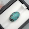 Premium 10.40 carat natural Egyptian turquoise (Feroza) oval cabochon displaying a vivid sky-blue body with an intricate, dark chocolate-brown spiderweb matrix, shown in a black jeweler's box.
