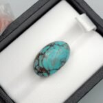 Premium 10.40 carat natural Egyptian turquoise (Feroza) oval cabochon displaying a vivid sky-blue body with an intricate, dark chocolate-brown spiderweb matrix, shown in a black jeweler's box.