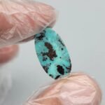Vibrant 5.80 carat natural Egyptian turquoise (Feroza) elongated oval cabochon with a bright teal-blue body and large, concentrated dark brown iron-rich matrix "islands".