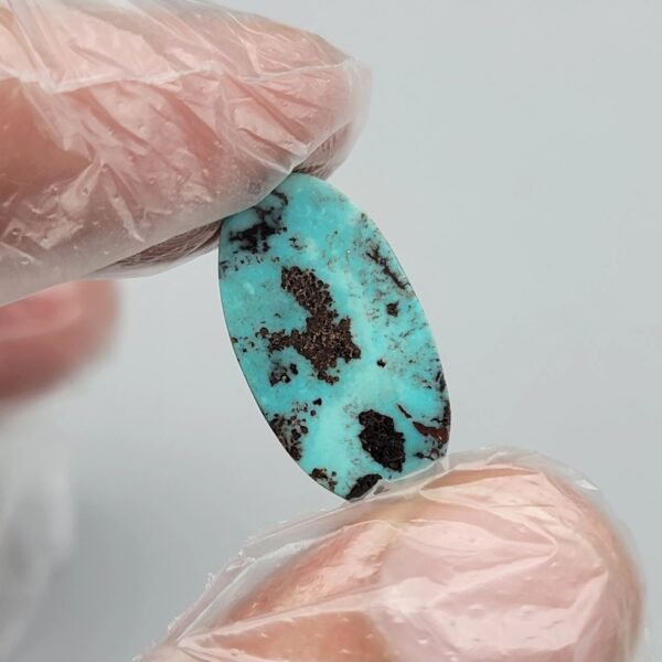 Vibrant 5.80 carat natural Egyptian turquoise (Feroza) elongated oval cabochon with a bright teal-blue body and large, concentrated dark brown iron-rich matrix "islands".