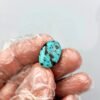 An 8.91 carat natural Egyptian turquoise (Feroza) oval cabochon featuring a brilliant sky-blue body with dark, irregular iron stone matrix patches, held in a gloved hand.