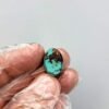 An 8.91 carat natural Egyptian turquoise (Feroza) oval cabochon featuring a brilliant sky-blue body with dark, irregular iron stone matrix patches, held in a gloved hand.