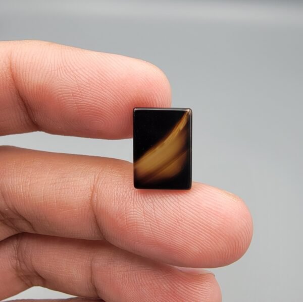 A 5.20 carat natural Black Agate (Sulemani Aqeeq) with a unique white foam pattern resembling wings, held in tweezers against a dark background.