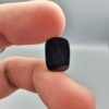 A 4.97 carat natural Black Agate (Sulemani Aqeeq) gemstone with a glossy oval cabochon cut, held in jeweler's tweezers against a dark background.