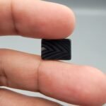 A 5.25 carat natural Black Agate (Sulemani Aqeeq) gemstone with an expertly polished oval cabochon cut, held in tweezers to showcase its high-luster surface and deep black color.