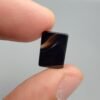A 5.29 carat natural Black Agate (Sulemani Aqeeq) gemstone with a high-gloss oval cabochon cut, held in tweezers to showcase its dense black color and light-reflective surface.