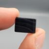 A 5.32 carat natural Black Agate (Sulemani Aqeeq) gemstone featuring a deep black, high-gloss oval cabochon cut, held in jeweler's tweezers against a dark professional background.