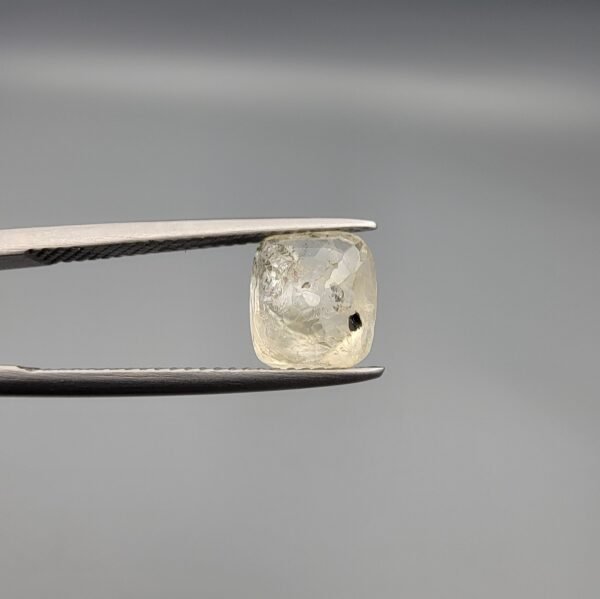 A 3.00 carat natural yellow sapphire (Pukhraj) held in tweezers, showing an oval cushion cut with visible mountain-like black inclusions on the reverse side against a grey background.