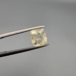 A 3.00 carat natural yellow sapphire (Pukhraj) held in tweezers, showing an oval cushion cut with visible mountain-like black inclusions on the reverse side against a grey background.
