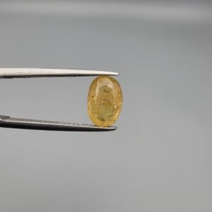 A 2.68 carat natural lemon yellow sapphire (Pukhraj) from Sri Lanka held in tweezers, featuring a brilliant oval cut and transparent clarity against a neutral grey background.