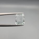 A 2.58 carat natural Aquamarine (Beruj) gemstone from Shigar Valley, Pakistan, featuring a crisp emerald cut and high transparency, held in jeweler's tweezers against a grey background.