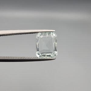 A 2.58 carat natural Aquamarine (Beruj) gemstone from Shigar Valley, Pakistan, featuring a crisp emerald cut and high transparency, held in jeweler's tweezers against a grey background.