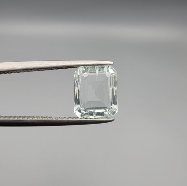 A 2.58 carat natural Aquamarine (Beruj) gemstone from Shigar Valley, Pakistan, featuring a crisp emerald cut and high transparency, held in jeweler's tweezers against a grey background.